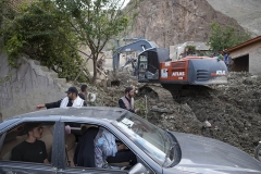 NPNW26JUL3122. An Iranian family drive their vehicle past the ruins of destroyed residential buildings as a bulldozer clear mud, in the flooded village of Mazdaran in Firoozkooh county 124 km (77 miles) northeast of Tehran, after flash flooding, July 31, 2022.