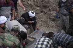 NPNW43AUG0322. An Iranian cleric prays as he sits next to a grave at a graveyard in the flooded village of Mazdaran in Firoozkooh county 124 km (77 miles) northeast of Tehran, during a funeral for flood victims, August 3, 2022.