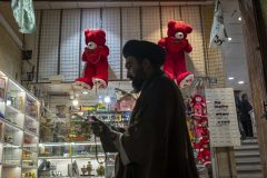 NPGR42MAR1022. An Iranian cleric walks past two red teddy bears hanged on a wall just out of a toy shop near a holy shrine in the holy city of Qom 145Km (90 miles) south of Tehran on March 10, 2022.